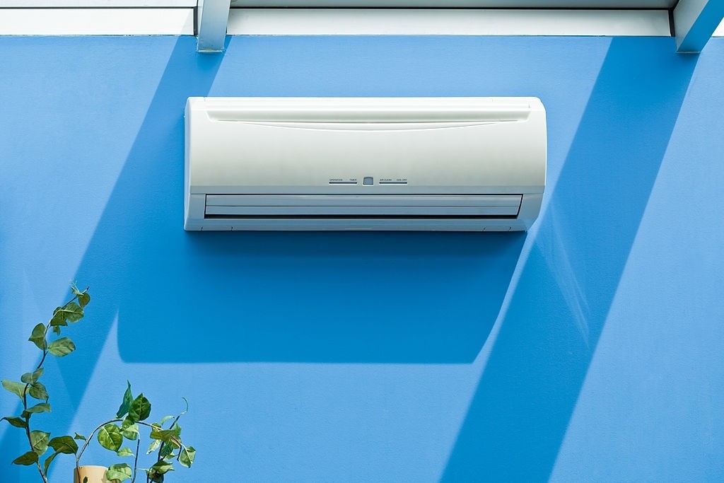 Ar condicionado branco em parede azul com folhas debaixo.