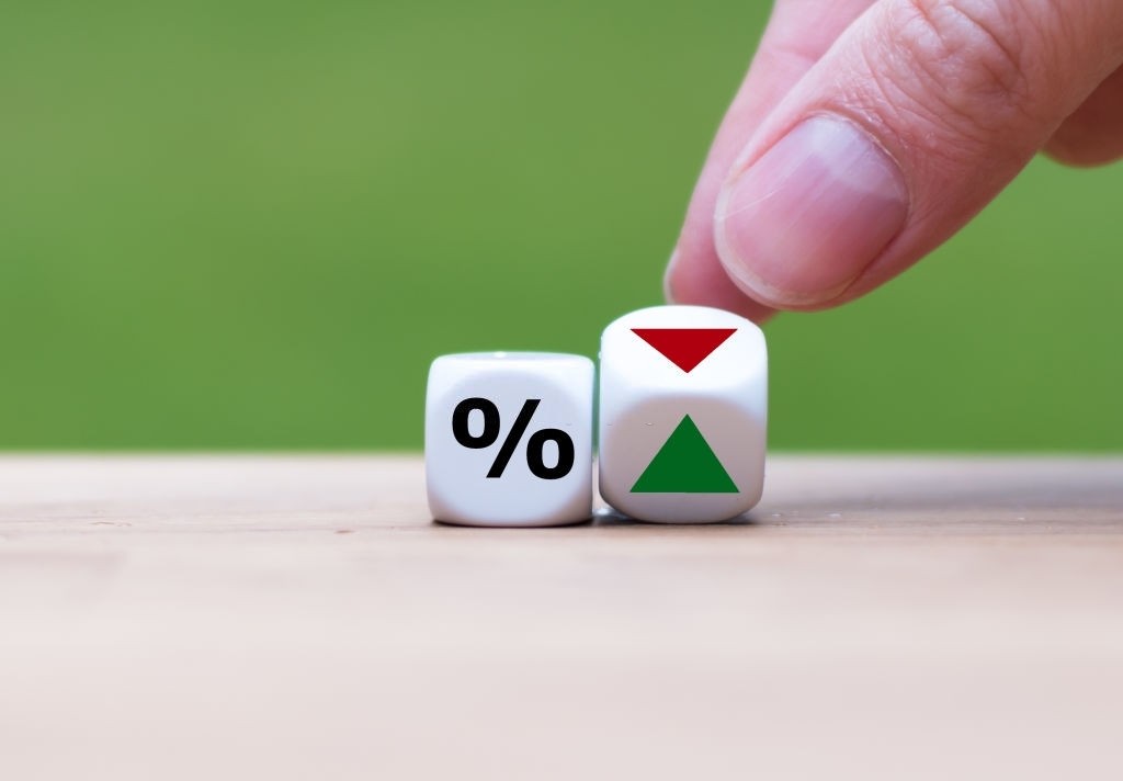 Dedos segurando um dado com duas setas: vermelha e verde, com outro dado ao lado com porcentagem em fundo verde.